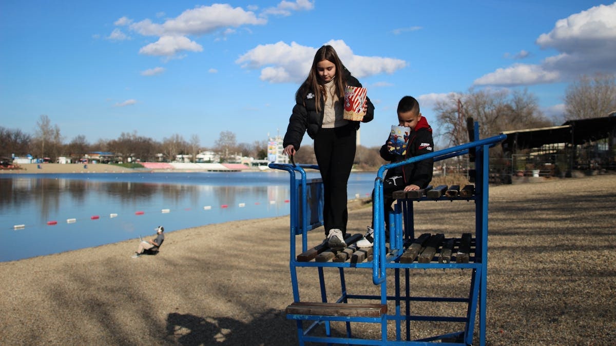 Two kids with popcorn by a lake, enjoying a sunny autumn day.
